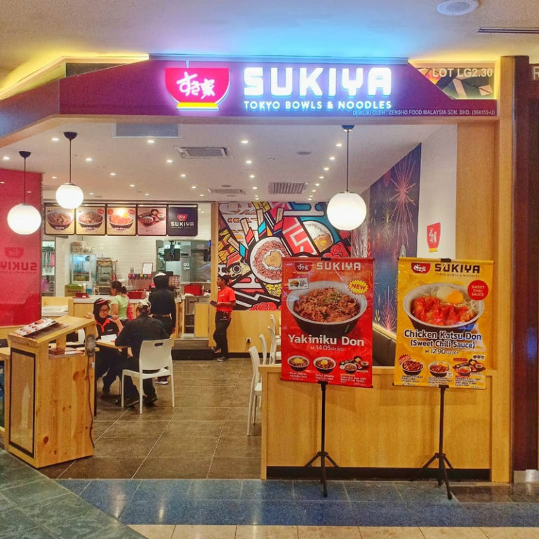 Interior Restoran Sukiya dengan mural berwarna-warni dan papan tanda promosi untuk Yakiniku Don dan Chicken Katsu Don, terletak di pusat beli-belah di Malaysia.